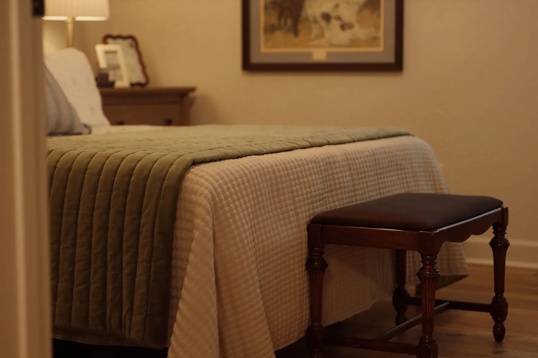 Bedroom with an olive quilted bed and a leather-topped bench in warm evening light