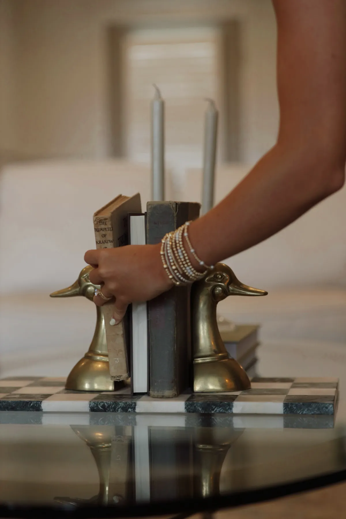 Hand placing brass bookends and taper candles on a glass coffee table