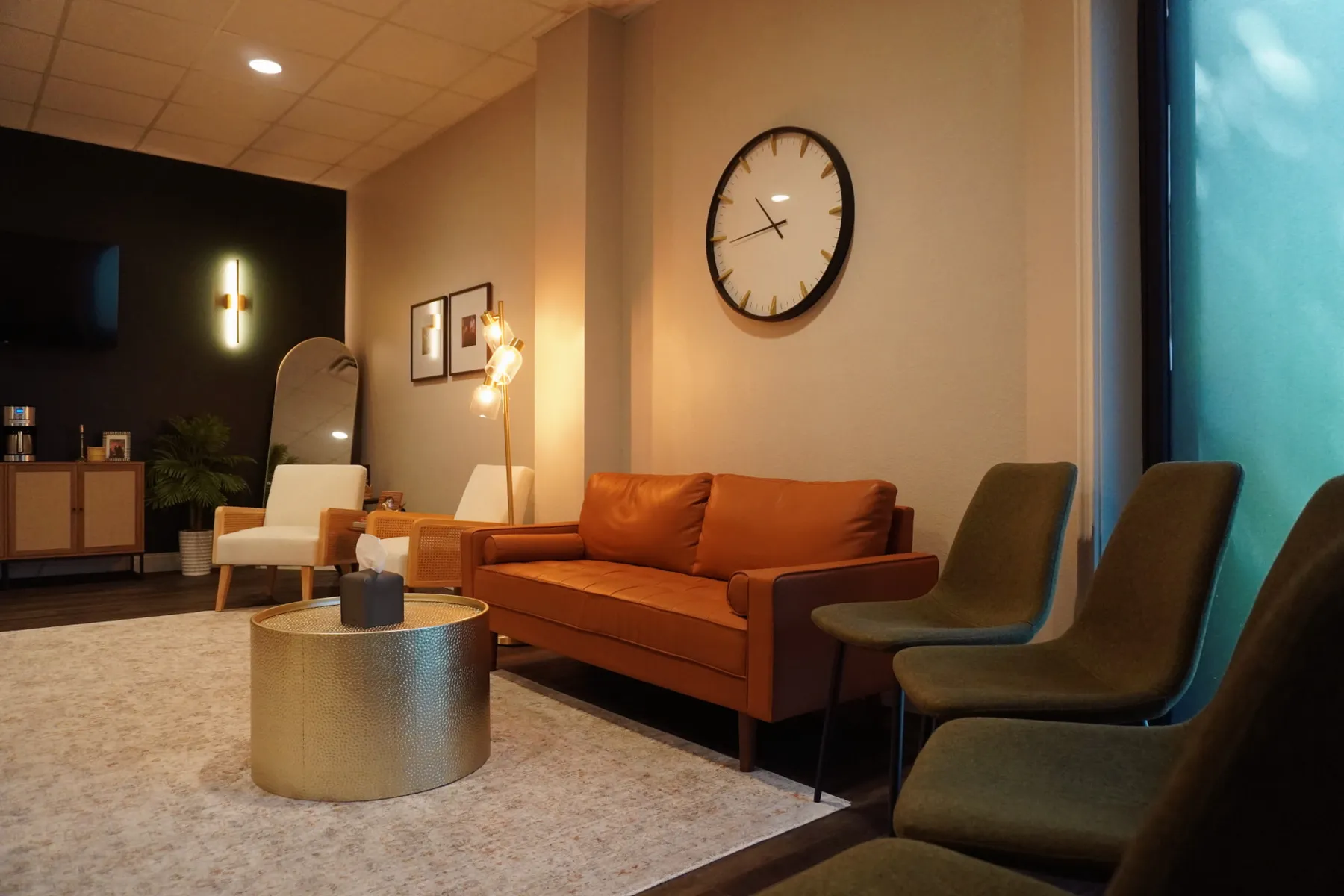Office waiting area with an orange sofa, olive chairs and a large wall clock