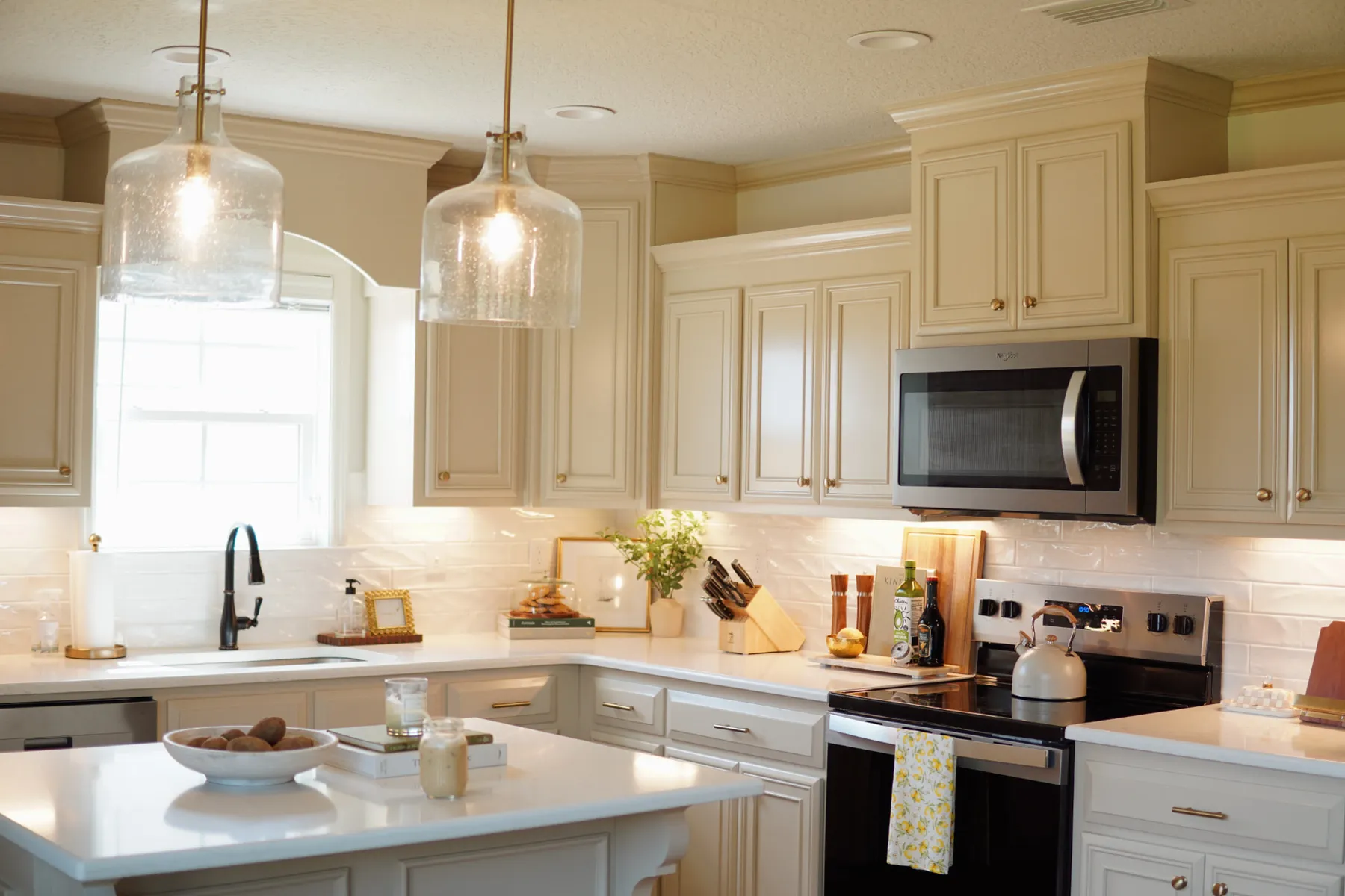 White kitchen with a center island, glass pendant lights and light stone counters