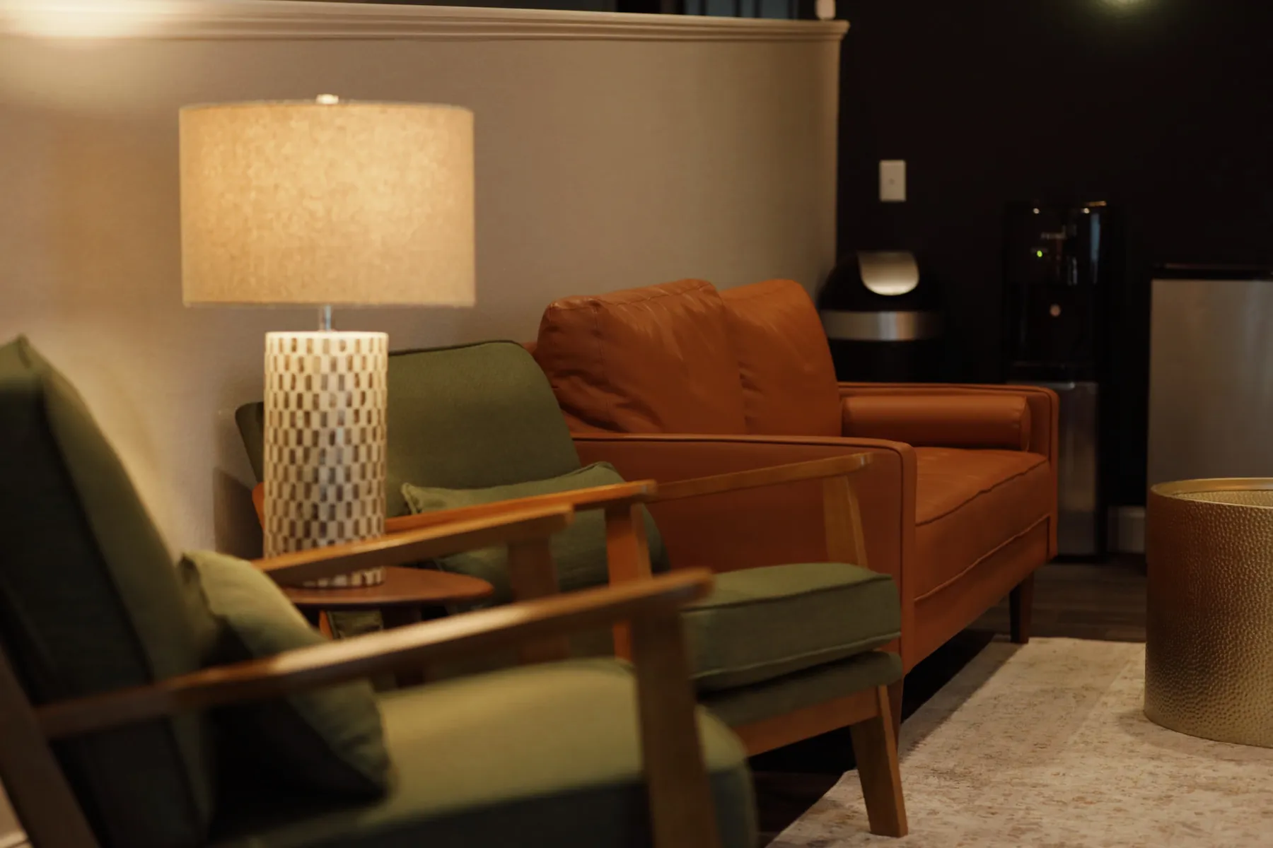 Office lounge with green mid-century chairs, a rust sofa and a lamp-lit corner