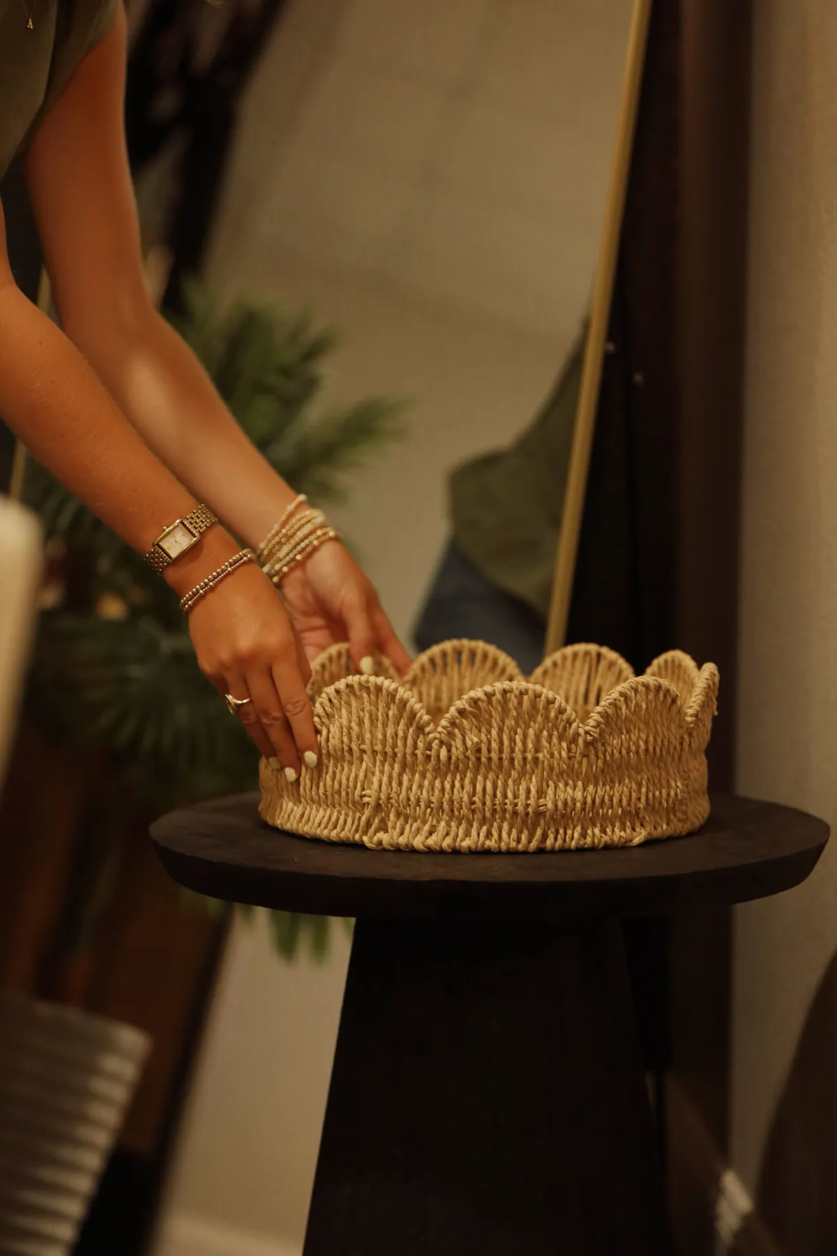Hand placing a scalloped rattan tray on a black pedestal table
