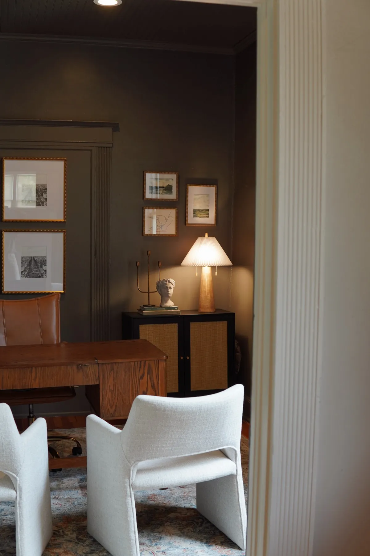 Office with a wood desk, sculptural white chairs and framed prints