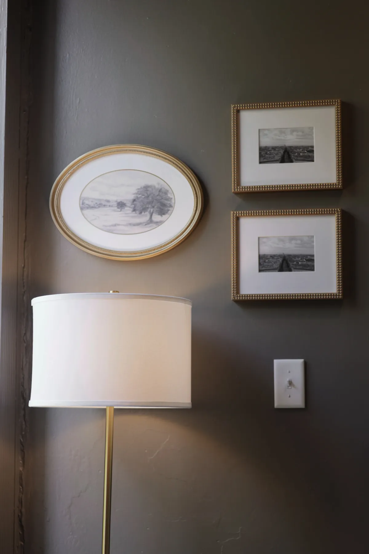 Brass floor lamp and framed landscape art on a deep green office wall