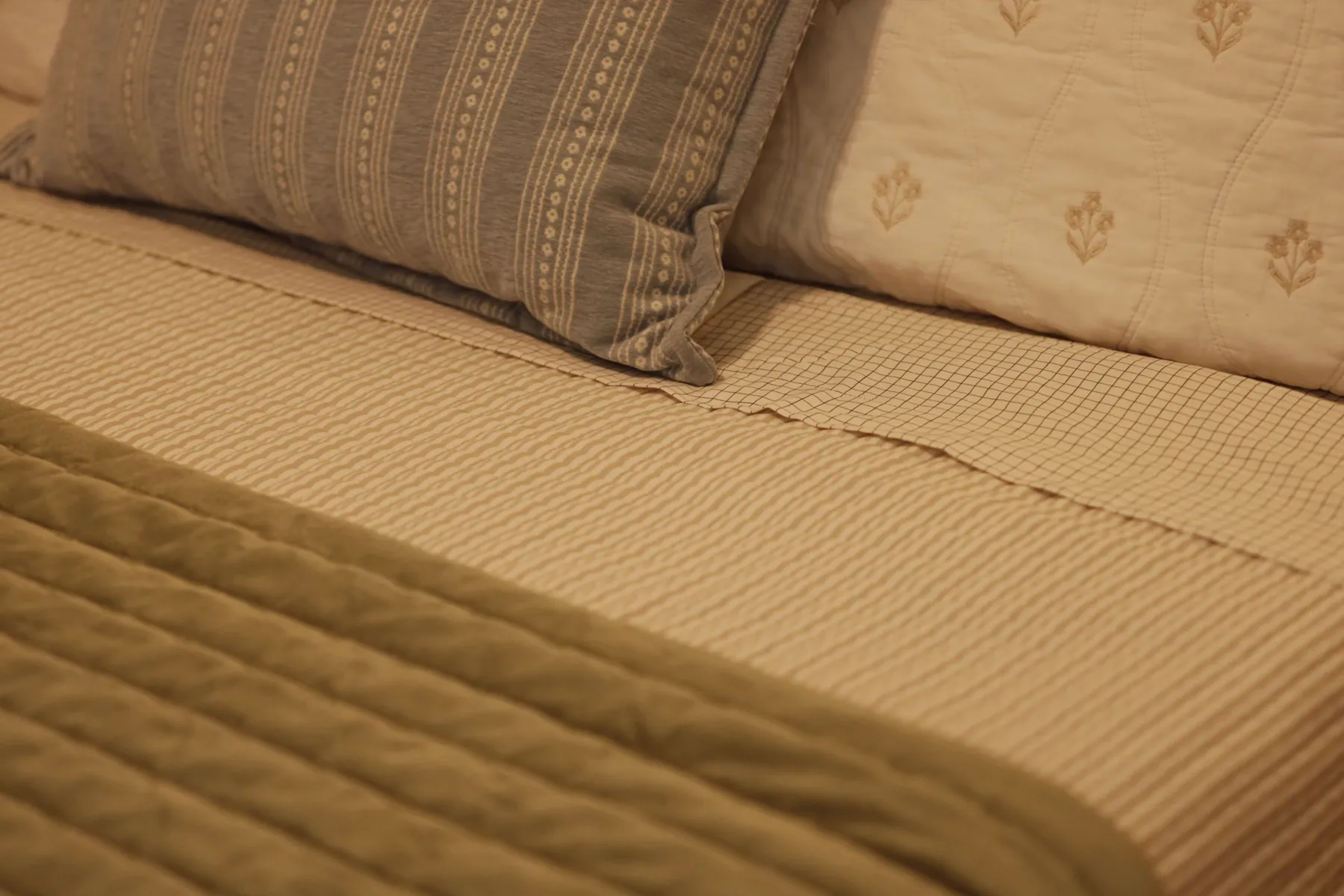 Close-up of quilted bedding layered with striped and patterned pillows