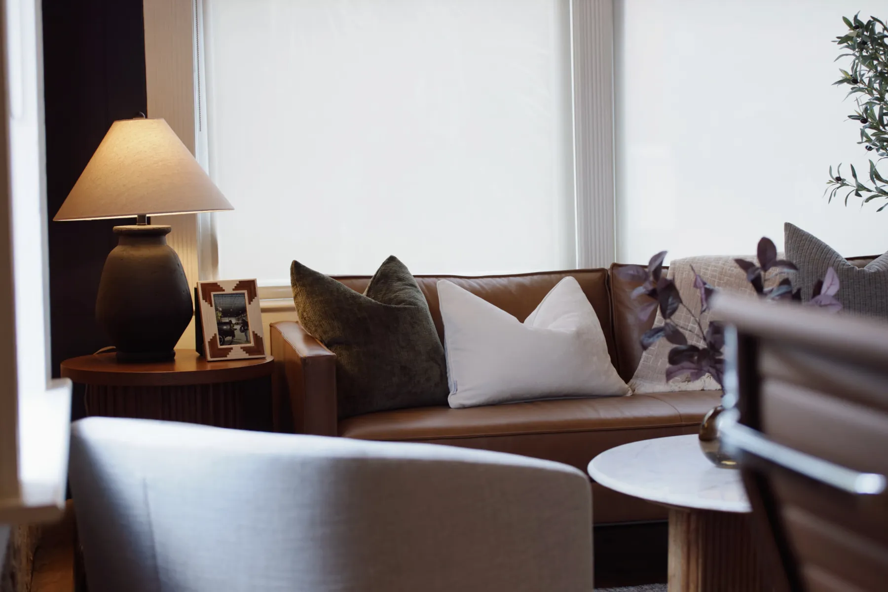 Office lounge with a leather sofa and a lamp-lit side table beside bright windows