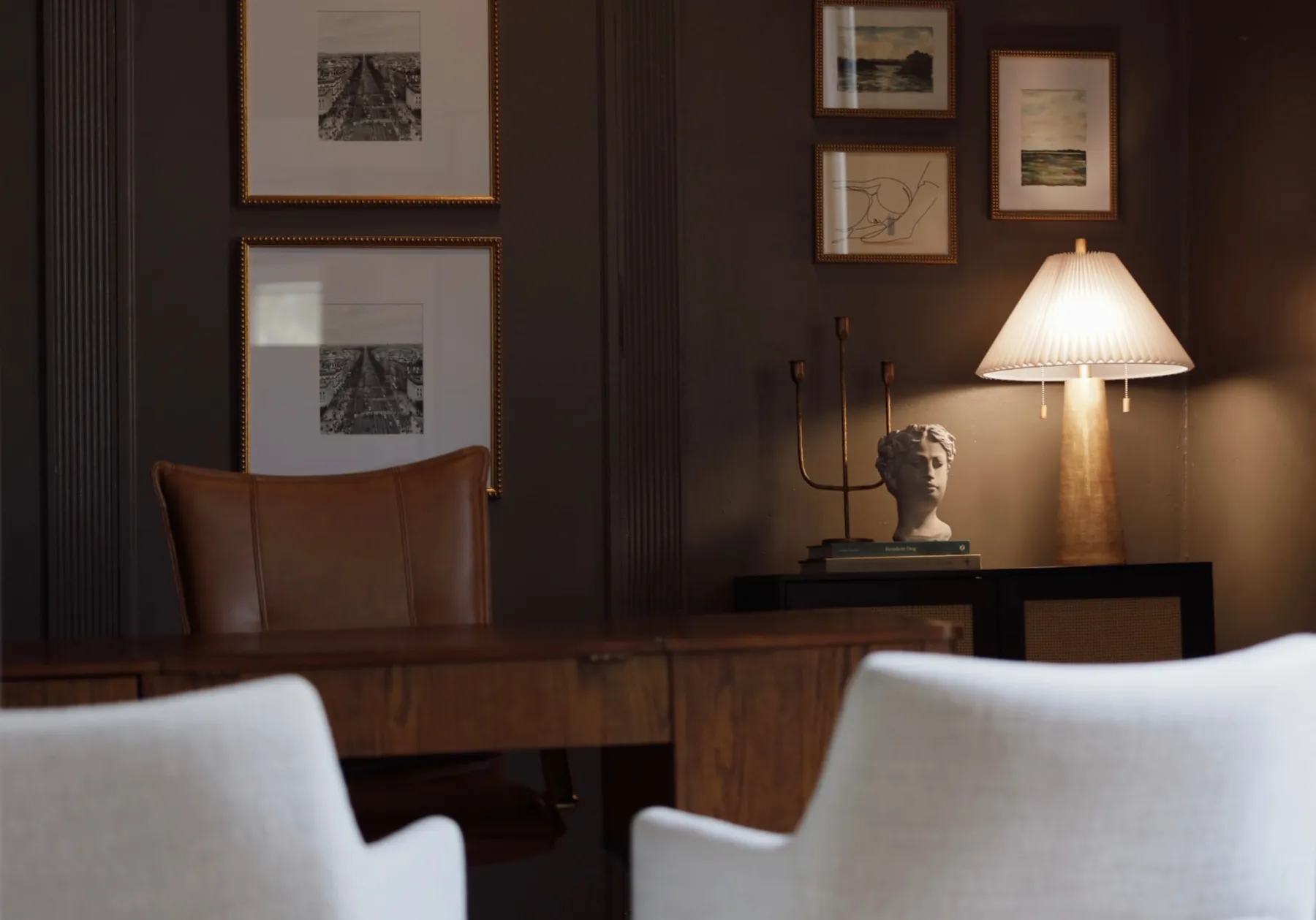 Dark-paneled office meeting room with framed prints, a table lamp and white chairs