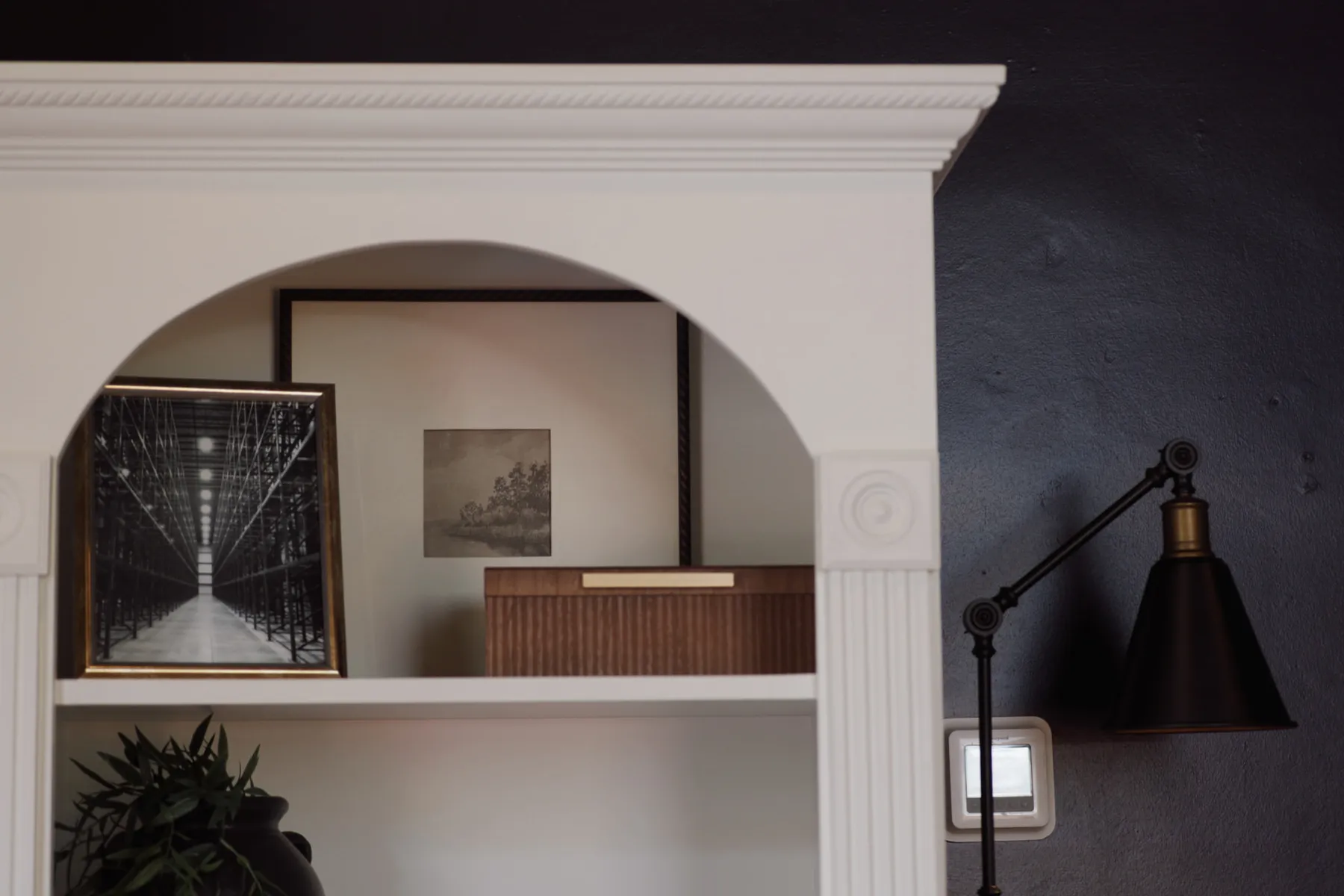 Arched white niche with framed prints, a black sconce and a potted plant