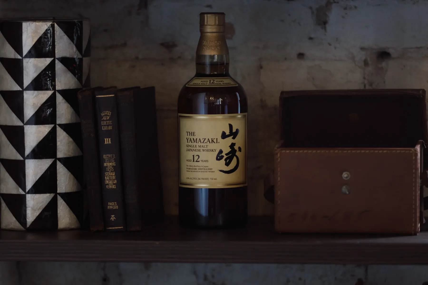 Styled office shelf with books, a leather box and a bottle of Japanese whisky