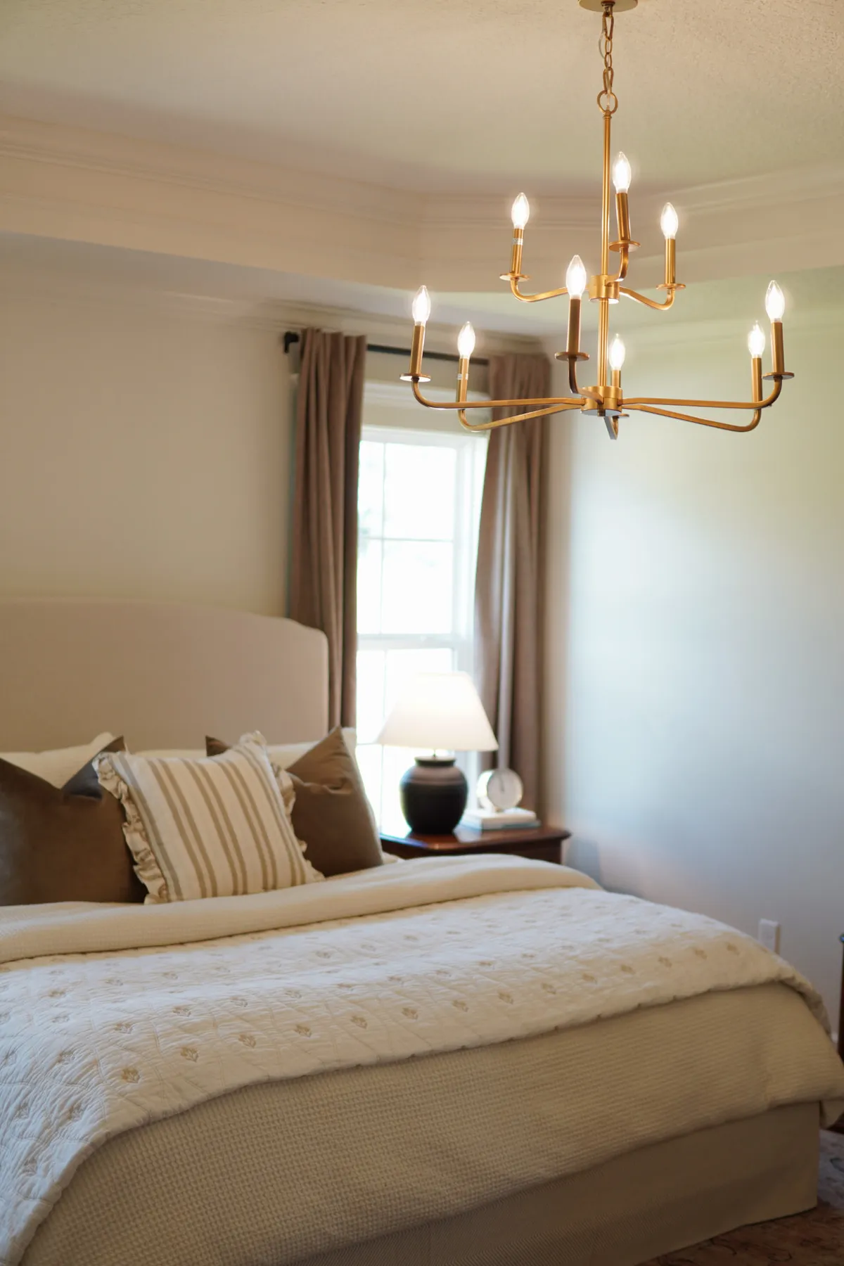 Bedroom with a brass chandelier above an ivory-layered bed and striped pillows