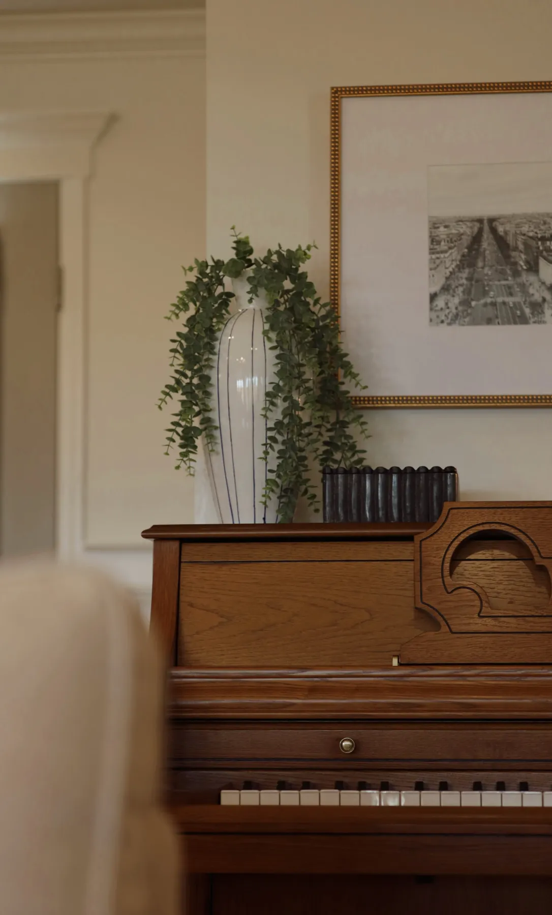 Antique oak upright piano styled with a trailing plant and a framed print