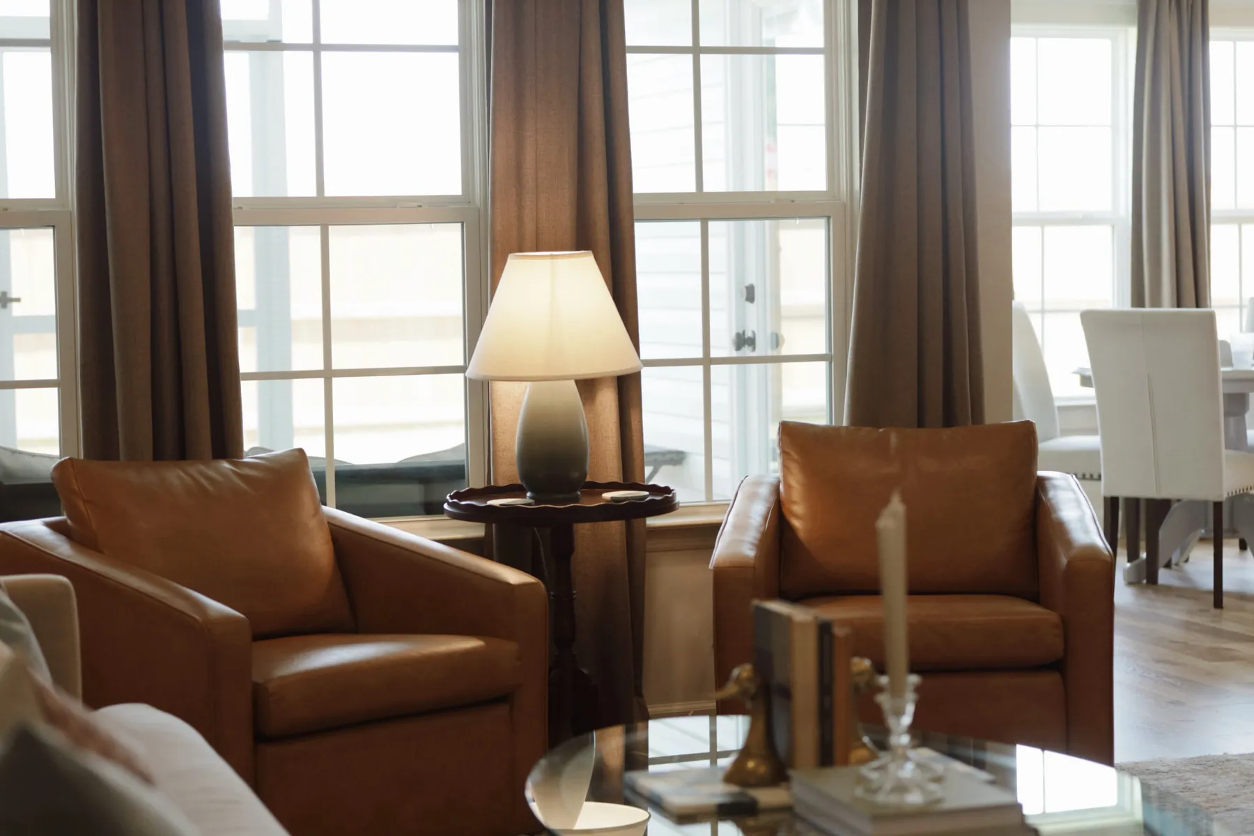 Living room with leather club chairs and a lamp-lit side table by curtained windows