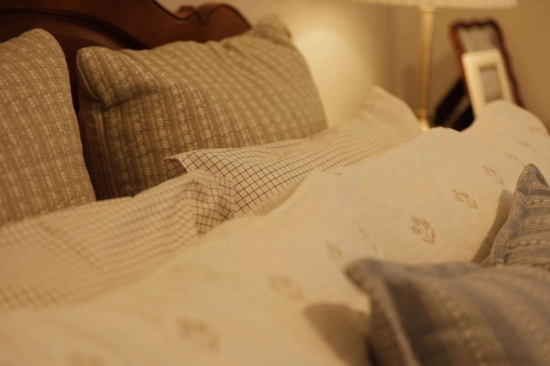 Bed layered with a green quilt and checked pillows in warm lamplight